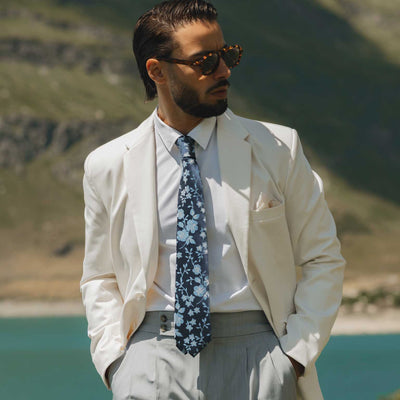 Man in a light suit with a blue floral tie standing in front of a mountainous landscape