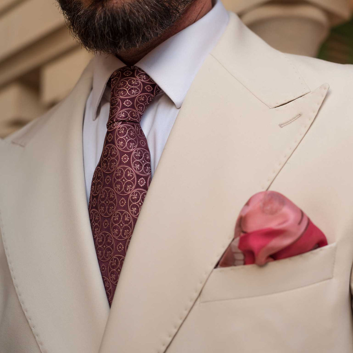 Man wearing a beige suit with a burgundy patterned tie and pocket square.