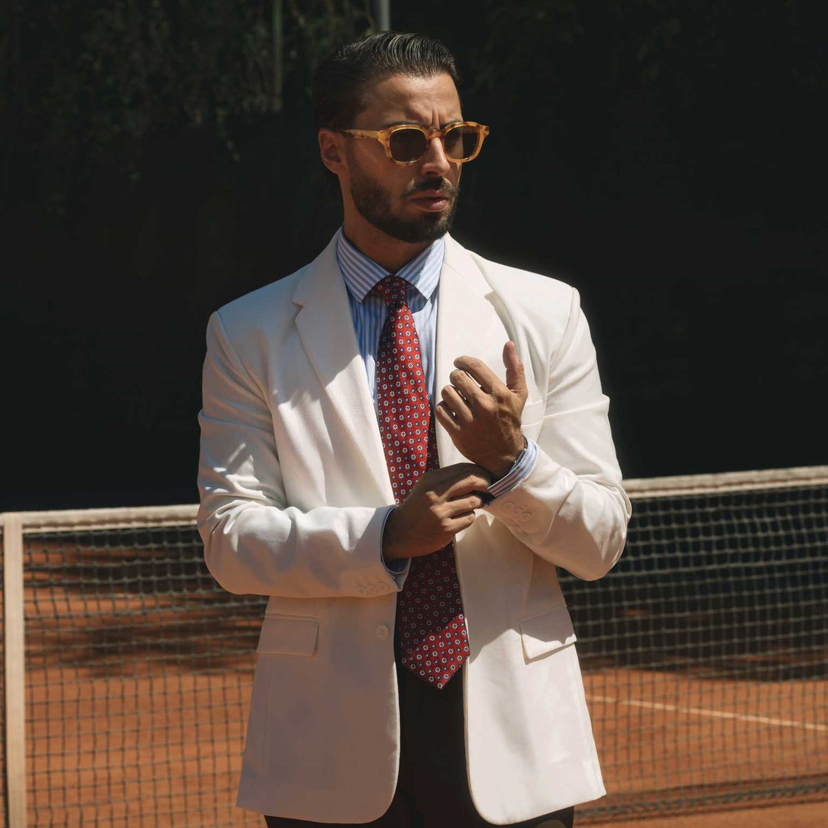 Man in a white suit and red tie on a tennis court